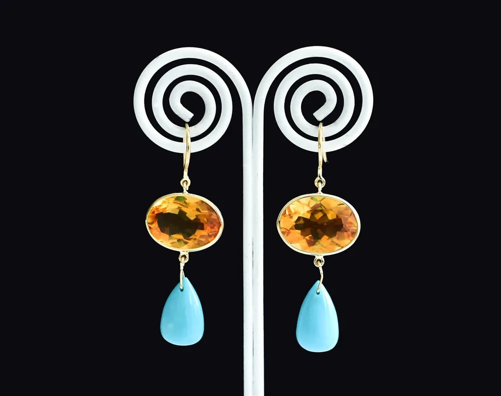 Citrine and turquoise drop earrings on a white spiral stand against a black background