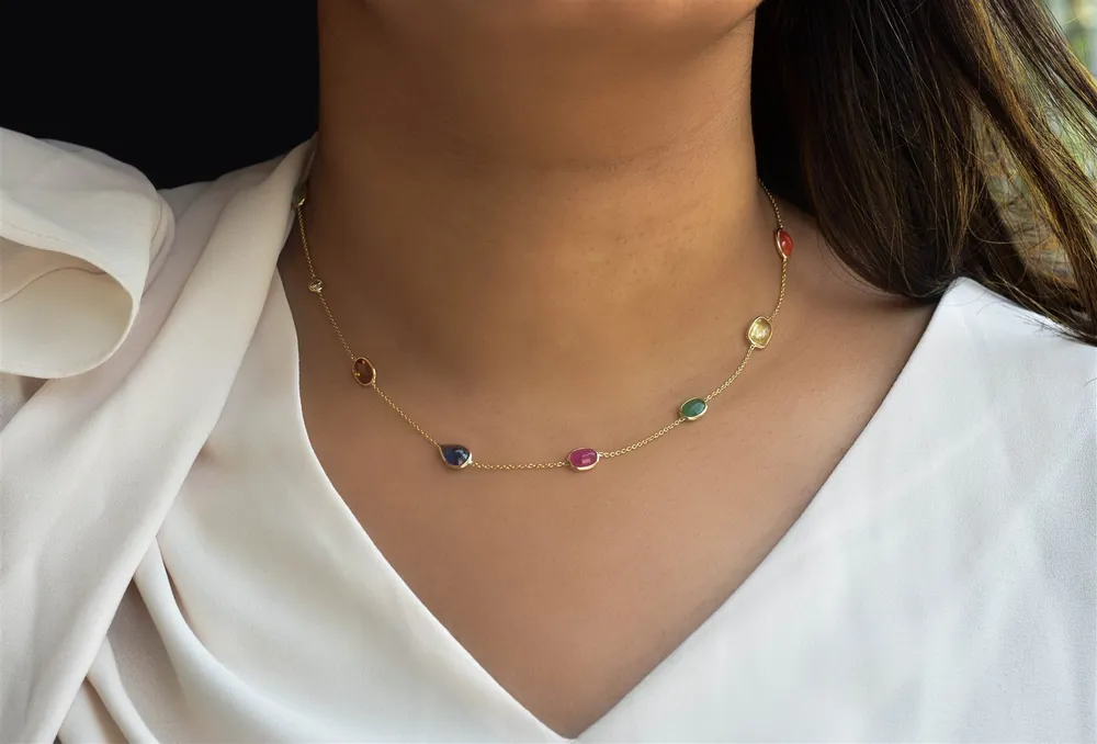 Delicate gold gemstone station necklace worn with a white top, on-model close-up