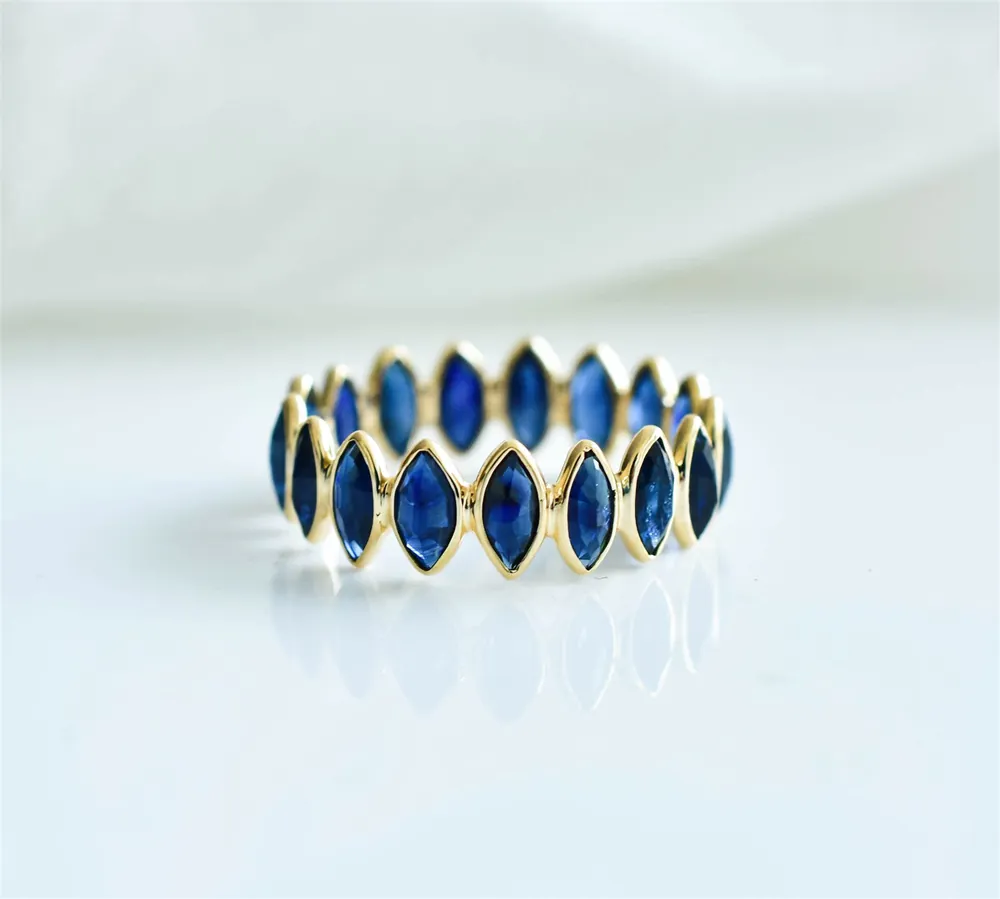 Blue sapphire marquise eternity band in gold on draped white fabric