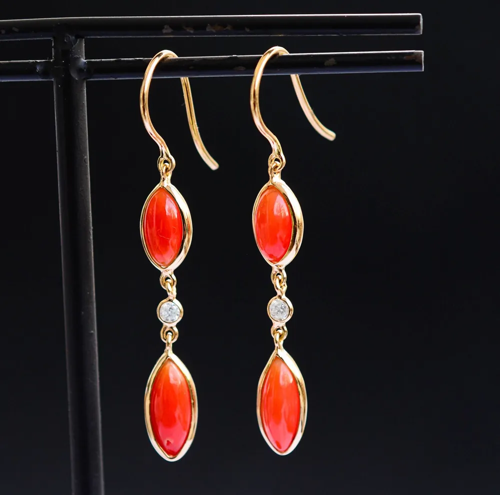 Coral and white topaz long drop earrings on a black display stand