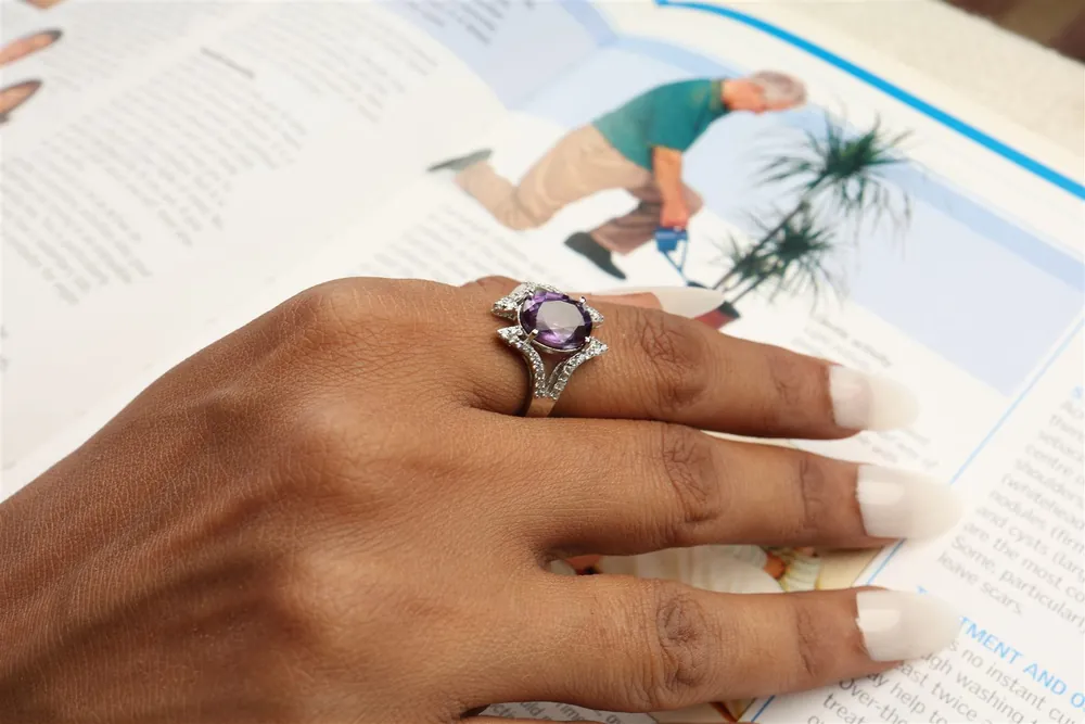 Hand wearing a gemstone cocktail ring resting on an open magazine, lifestyle shot