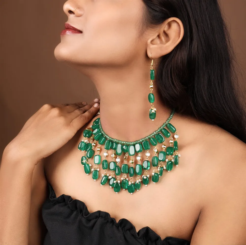 Model wearing a layered emerald bead bib necklace against a warm brown backdrop